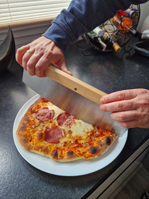 Profi Wiegemesser mit 35 cm Edelstahlklinge und Holzgriff beim mühelosen Schneiden einer frisch gebackenen Pizza in gleichmäßige Stücke.